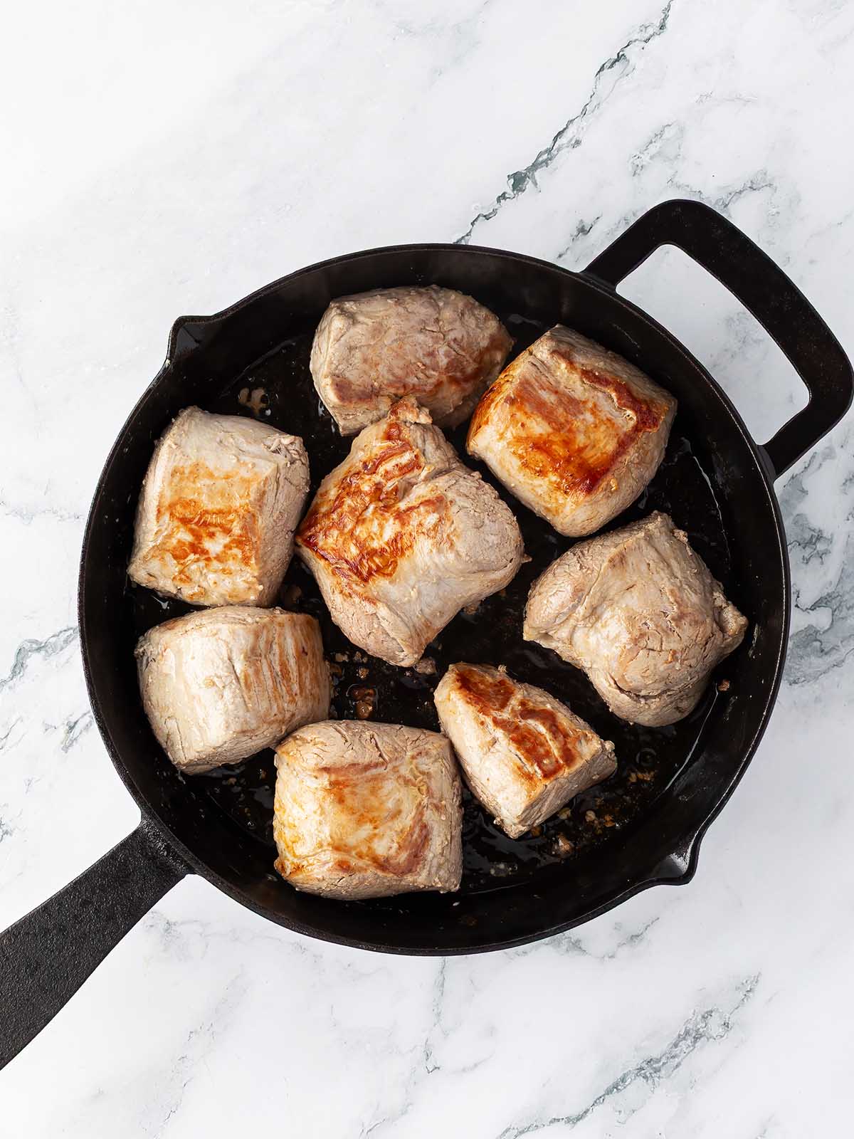 Seared chunks of pork in an iron skillet.