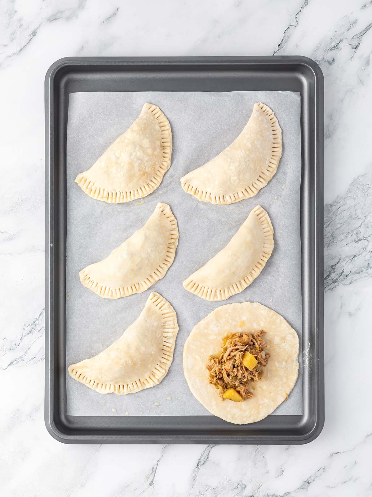 Making 6 unbaked empanadas on a baking tray.